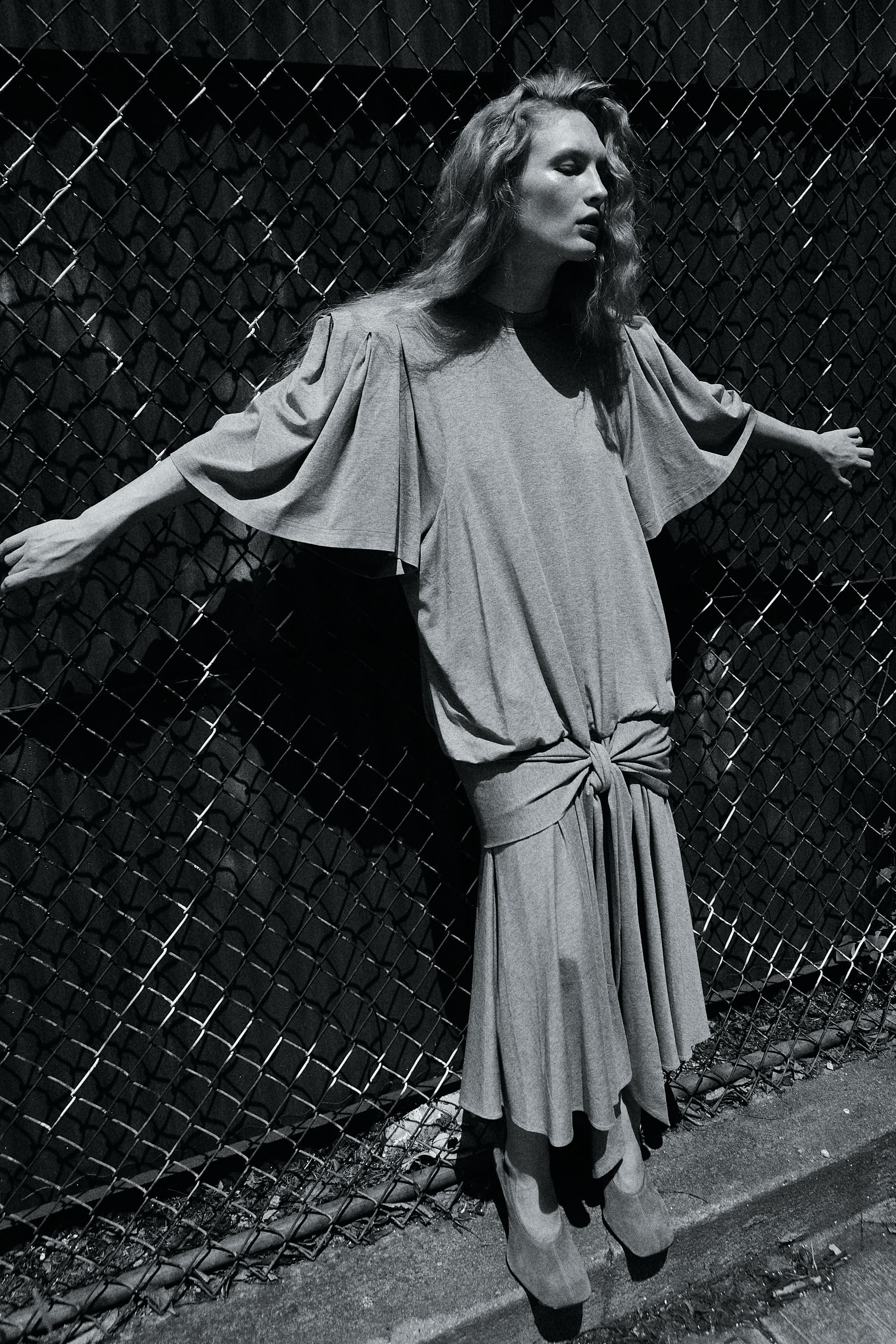Model in flowing grey dress against chain-link fence