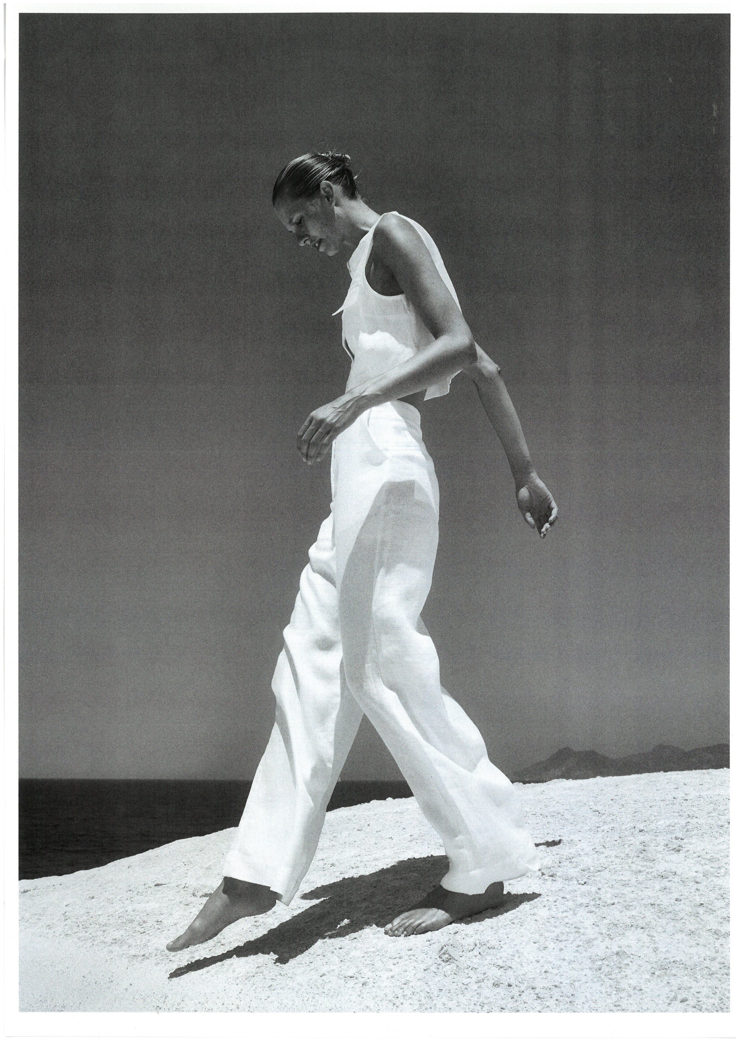 Black and white model walking on white sand in linen outfit