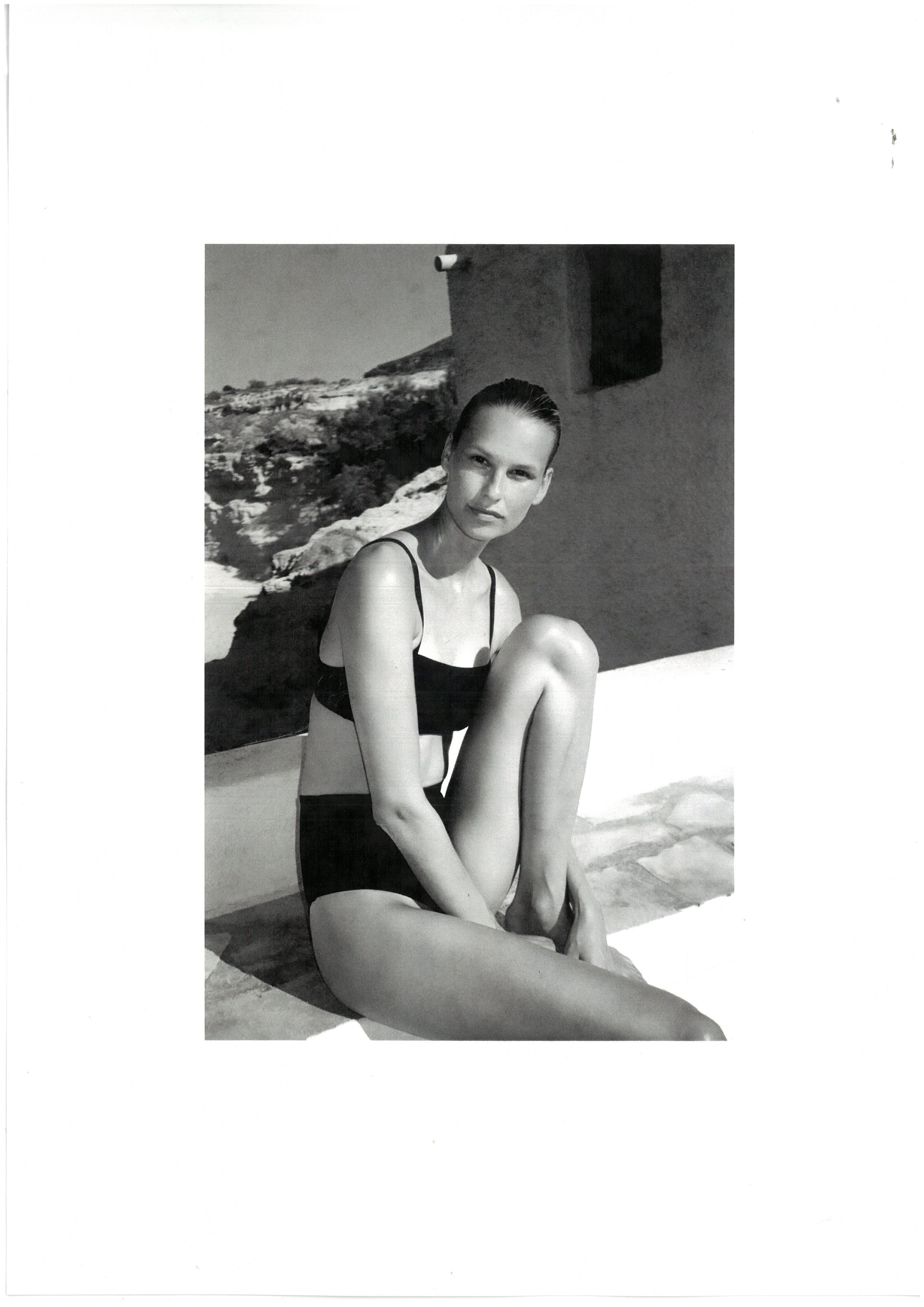 Black and white model in swimsuit sitting against wall